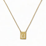 An Engraved Initial Necklace Letter U by Skōsh Jewelry, featuring a small rectangular tag engraved with the letter U on a fine gold chain, displayed against a white background.