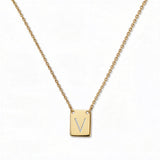 An Engraved Initial Necklace Letter V by Skōsh Jewelry, featuring a small rectangular tag engraved with the letter V on a fine gold chain, displayed against a white background.