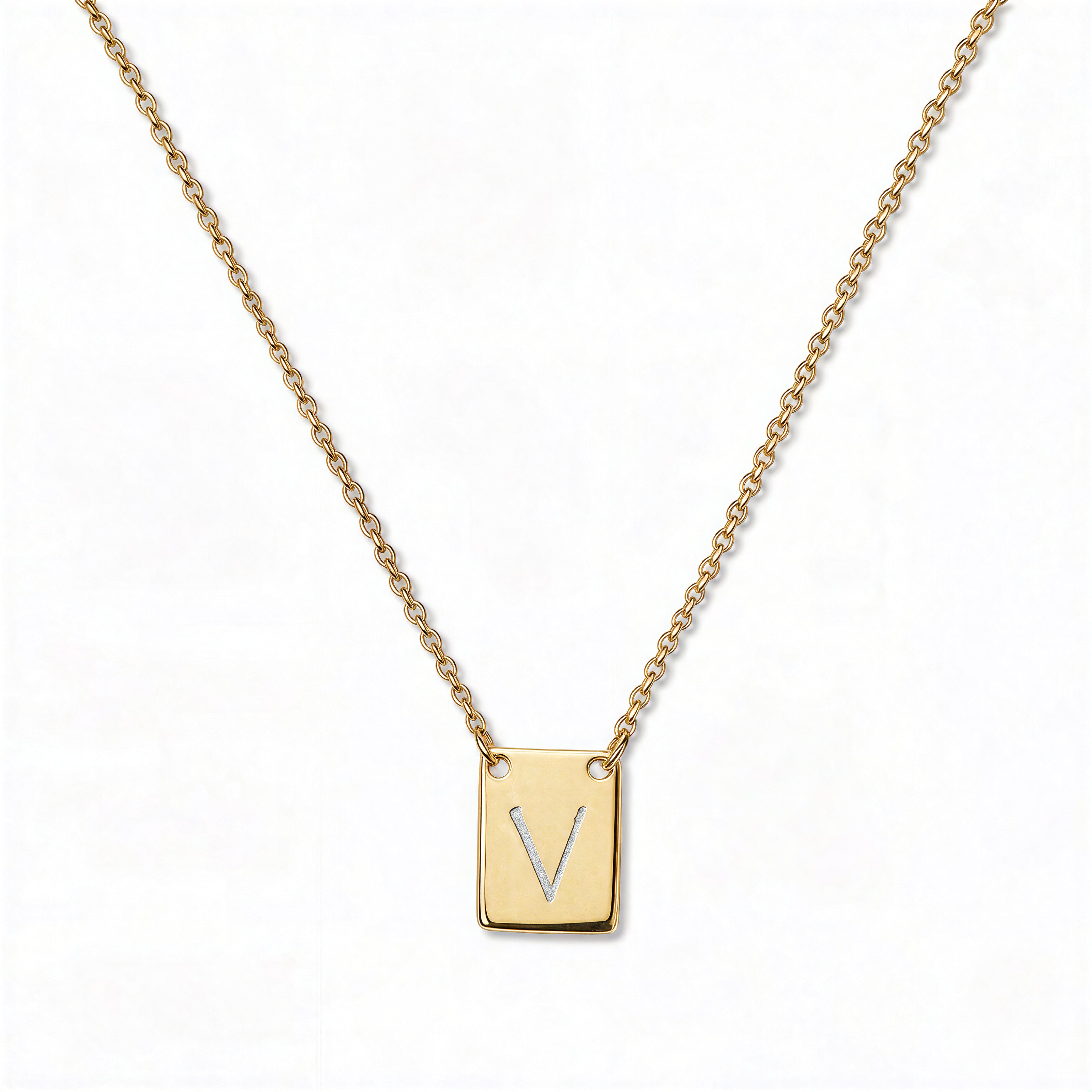 An Engraved Initial Necklace Letter V by Skōsh Jewelry, featuring a small rectangular tag engraved with the letter V on a fine gold chain, displayed against a white background.