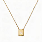 An Engraved Initial Necklace Letter X by Skōsh Jewelry, featuring a small rectangular tag engraved with the letter X on a fine gold chain, displayed against a white background.
