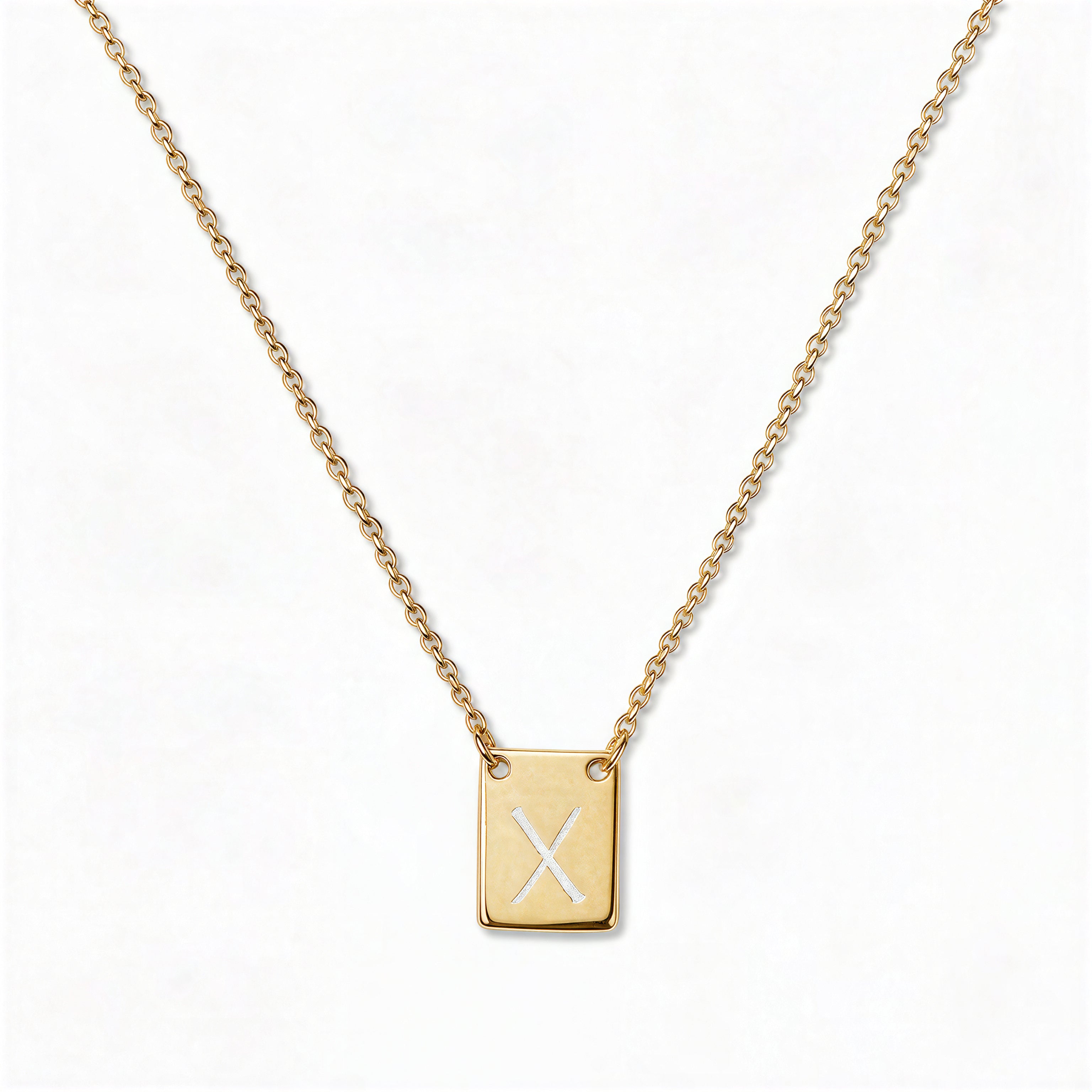 An Engraved Initial Necklace Letter X by Skōsh Jewelry, featuring a small rectangular tag engraved with the letter X on a fine gold chain, displayed against a white background.