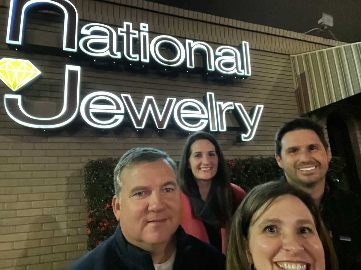 Group of friends taking a selfie in front of a National Jewelry storefront sign