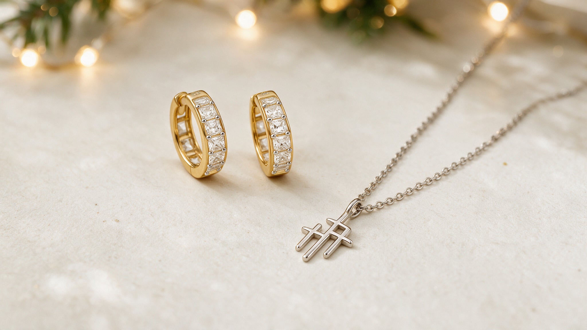 Gold baguette huggie hoop earrings and a sterling silver cross necklace by Skōsh Jewelry with holiday lights