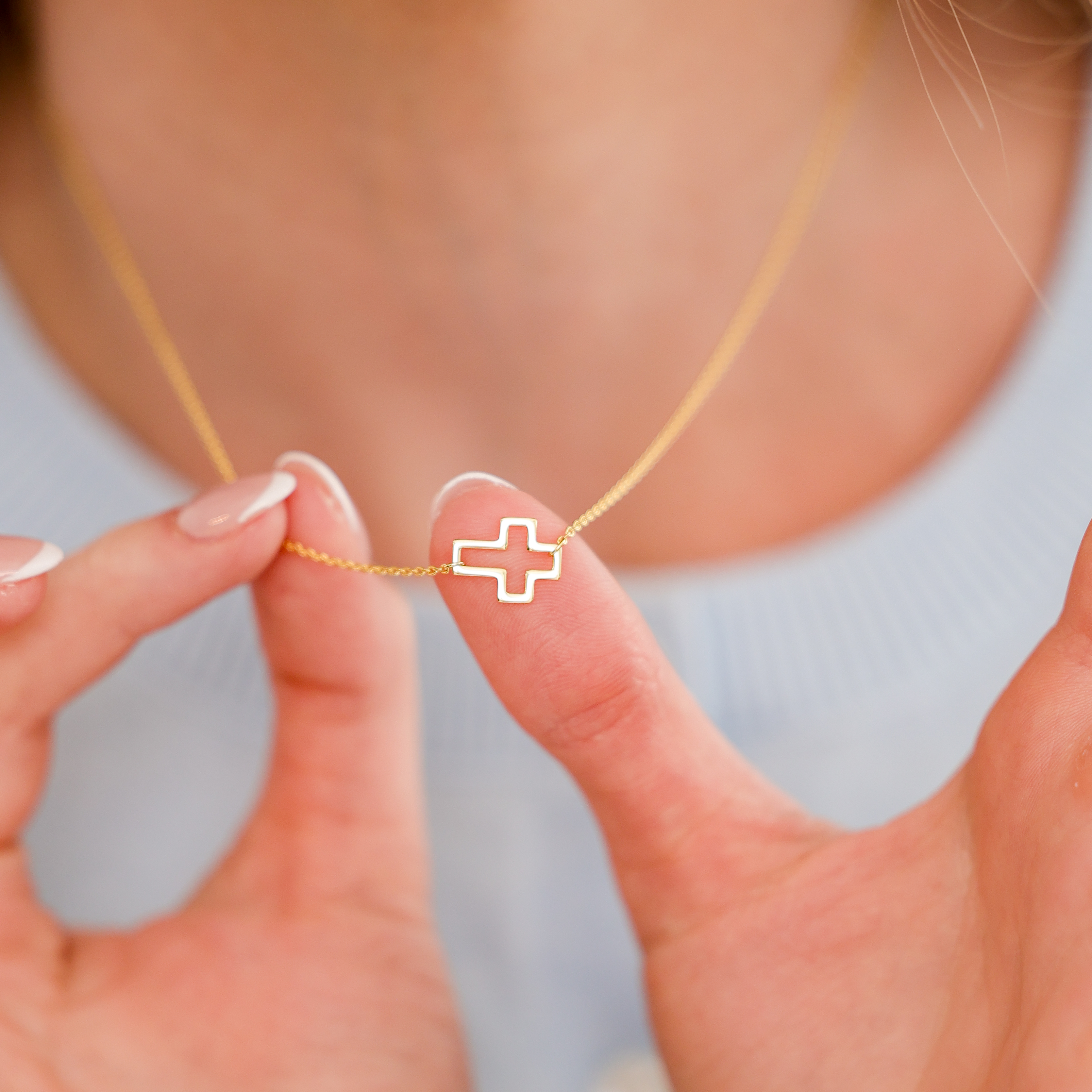 Woman holding a dainty pendant necklace by Skōsh Jewelry at her neckline